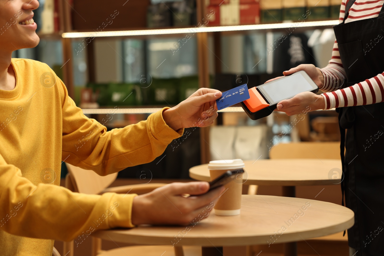 Photo of Man paying with credit card via terminal at wooden table in cafe, closeup