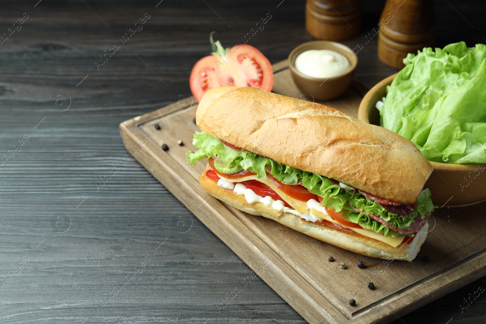 Photo of Delicious baguette sandwich with salami and cheese on grey wooden table. Space for text