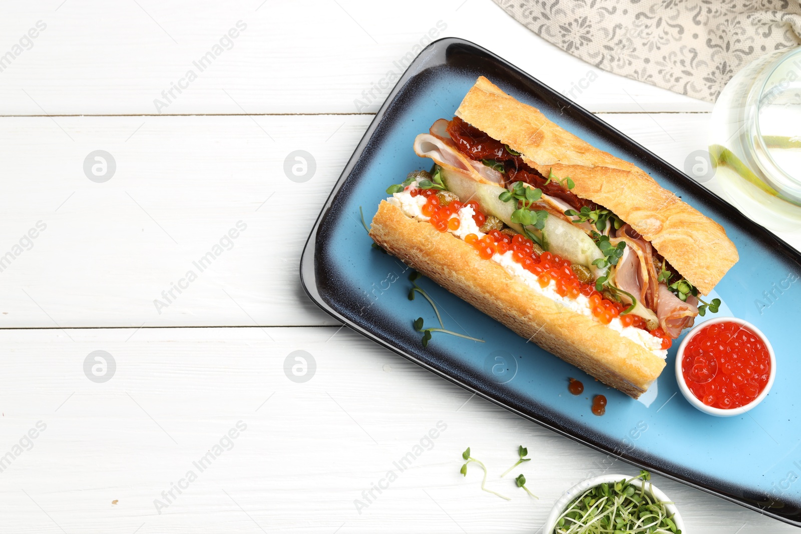 Photo of Delicious baguette sandwich with caviar, ham and capers on white wooden table, top view. Space for text