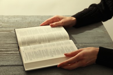 Photo of Woman with open Holy Bible in English language at wooden table, closeup