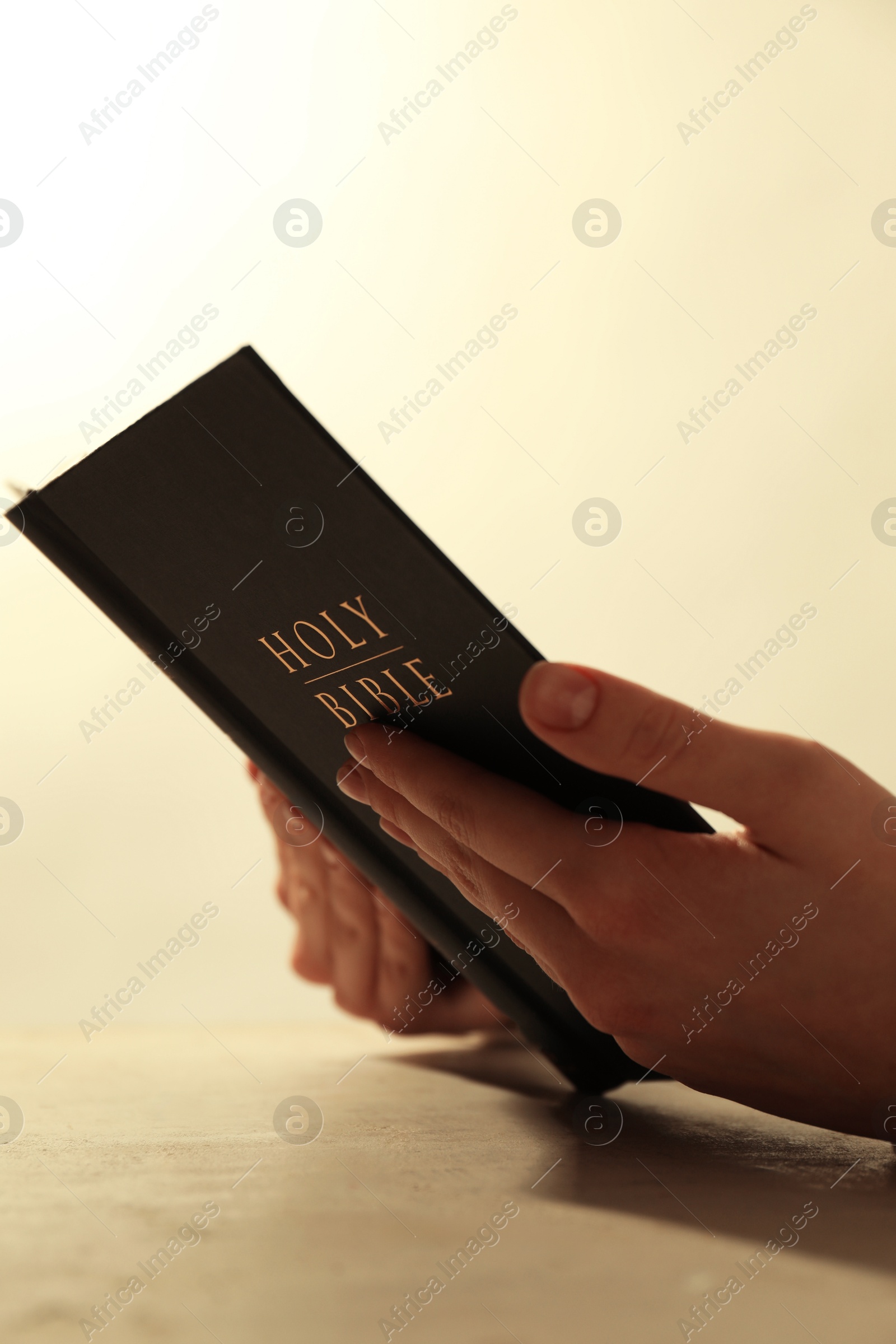 Photo of Woman reading Holy Bible at beige table, closeup