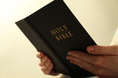 Woman reading Holy Bible against beige background, closeup