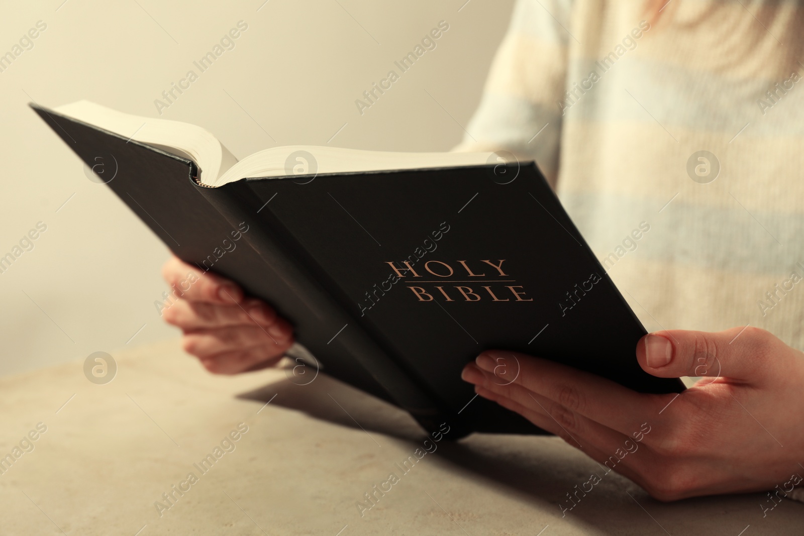 Photo of Woman reading Holy Bible at beige table, closeup