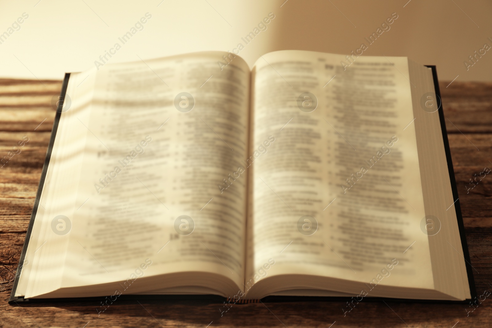 Photo of Open Holy Bible in English language on wooden table, closeup