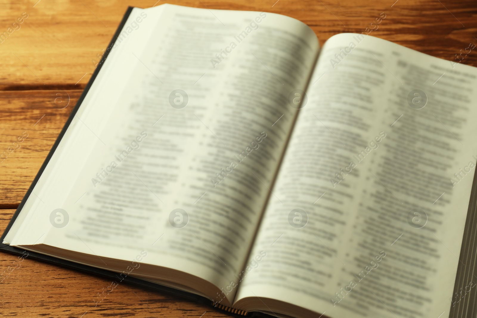 Photo of Open Holy Bible in English language on wooden table, closeup