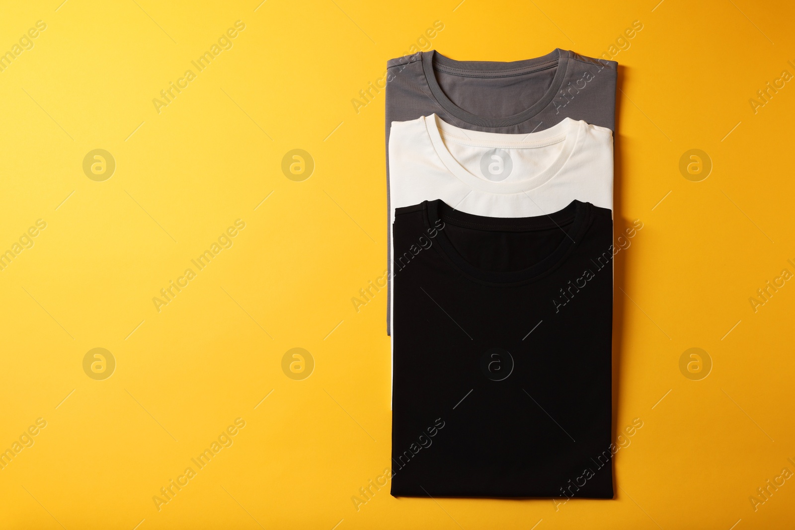 Photo of Different blank t-shirts on yellow background, top view. Mockup for design