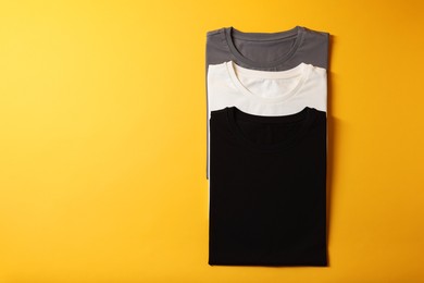 Photo of Different blank t-shirts on yellow background, top view. Mockup for design