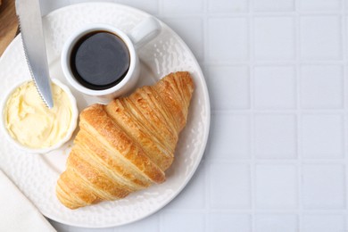 Photo of Tasty fresh croissant served with butter and cup of coffee on white tiled table, top view. Space for text