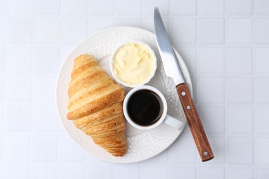 Photo of Tasty fresh croissant served with butter and cup of coffee on white tiled table, top view