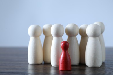 Photo of Human resources concept. Red figure among wooden ones on table against light background, closeup