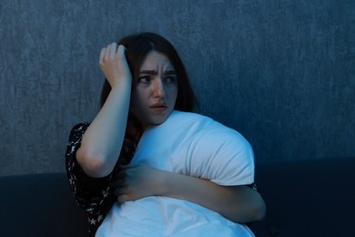 Photo of Fear of darkness. Scared young woman hugging pillow on couch indoors at night