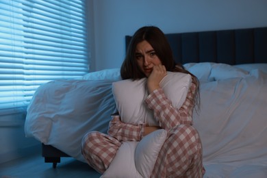 Photo of Fear of darkness. Scared young woman hugging pillow in bedroom at night