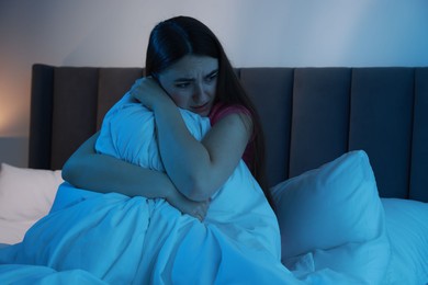 Photo of Fear of darkness. Scared young woman on bed in room at night