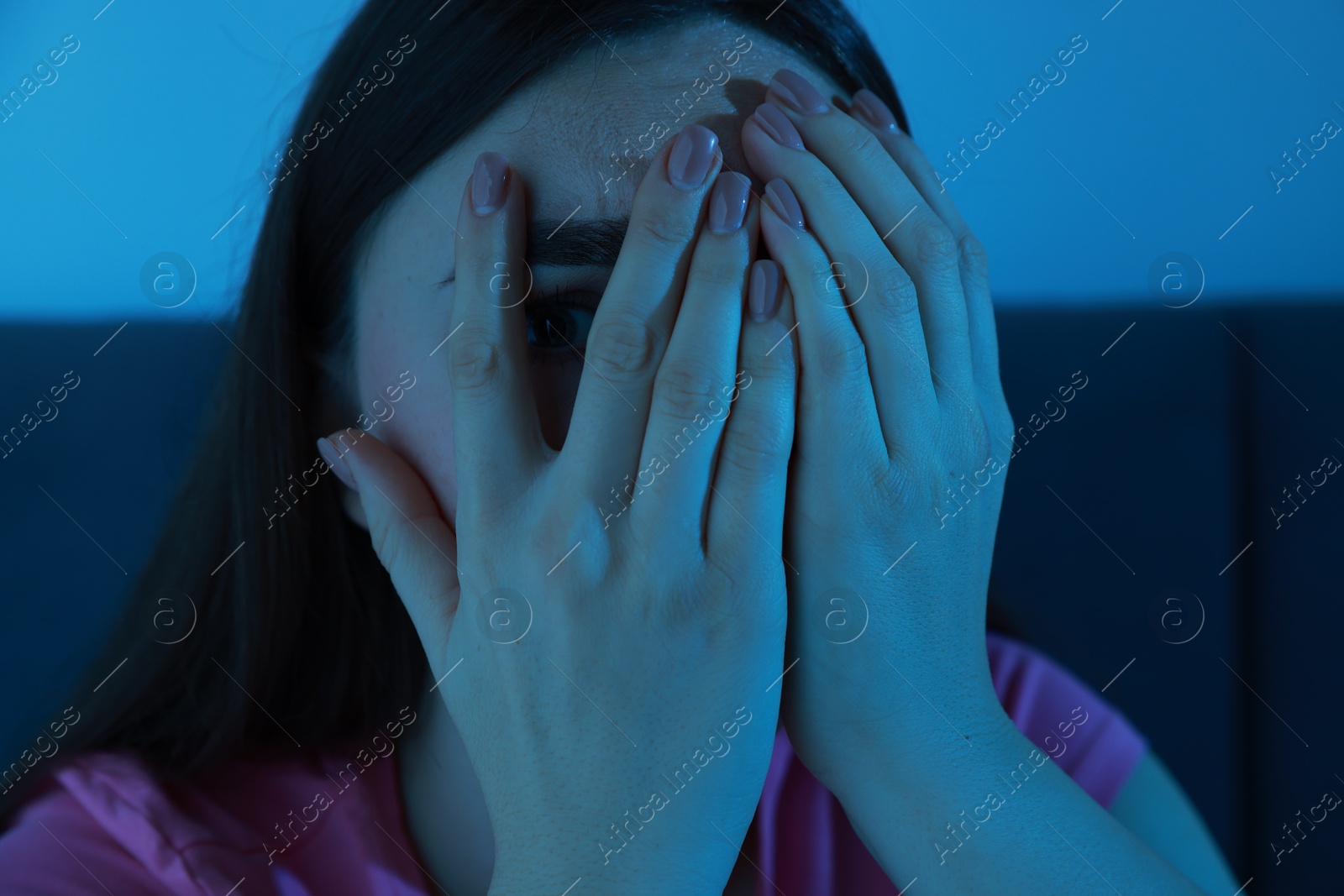 Photo of Fear of darkness. Scared young woman on bed and hiding her face in room at night