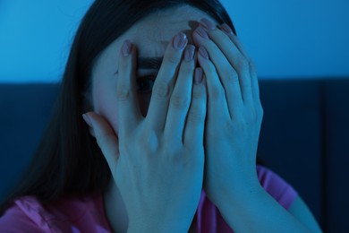 Photo of Fear of darkness. Scared young woman on bed and hiding her face in room at night