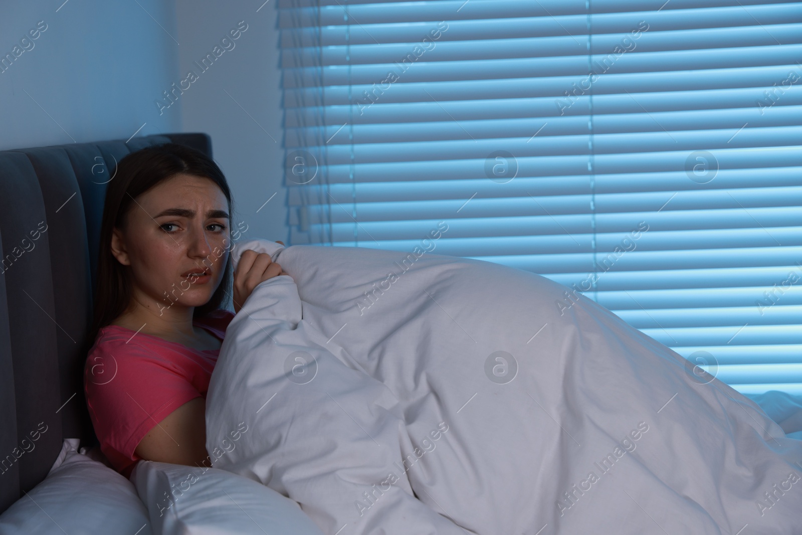 Photo of Fear of darkness. Scared young woman lying on bed in room at night, space for text