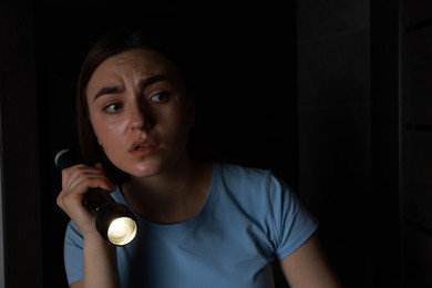 Photo of Fear of darkness. Scared young woman with flashlight indoors at night