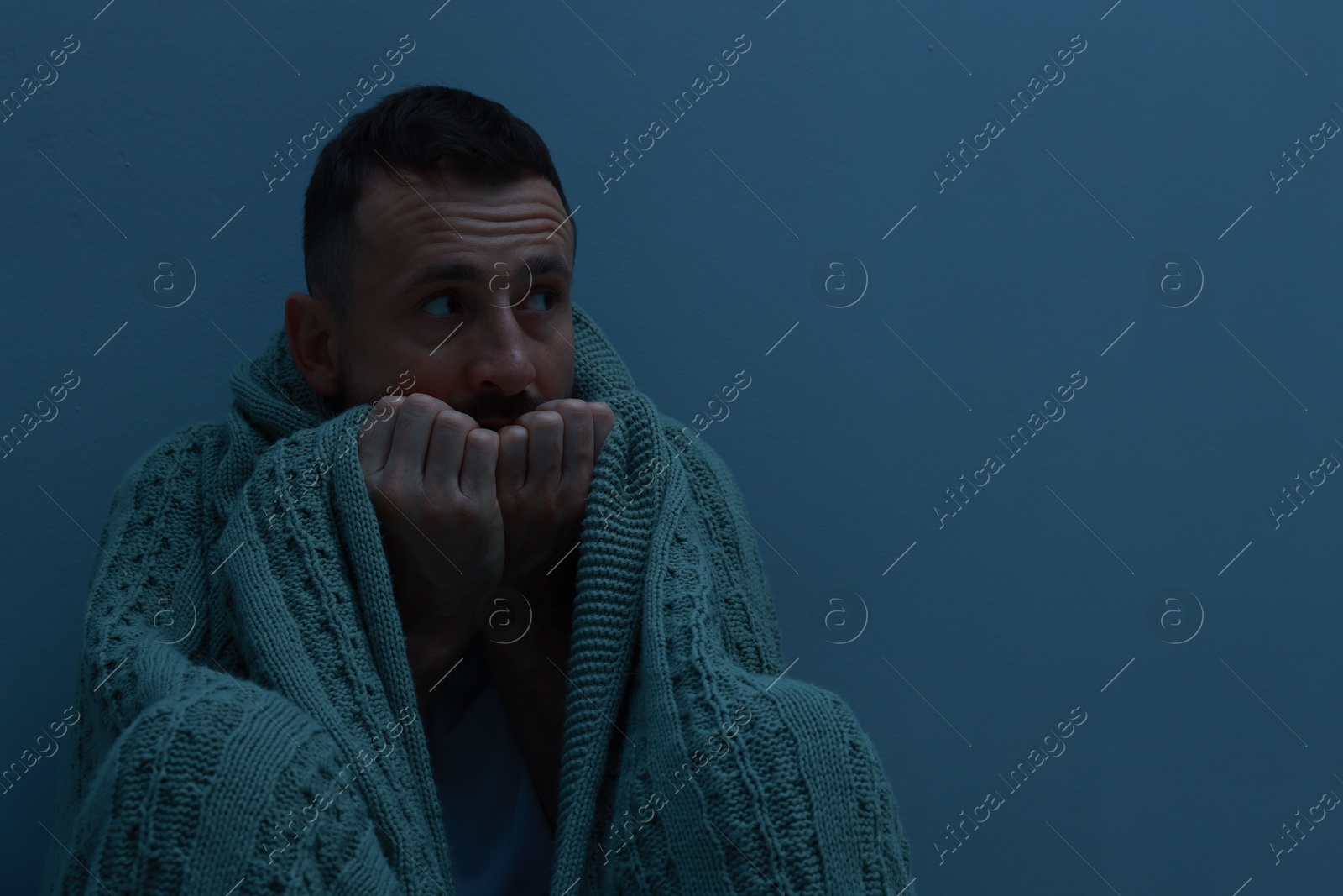 Photo of Fear of darkness. Scared man with blanket on light grey background, space for text