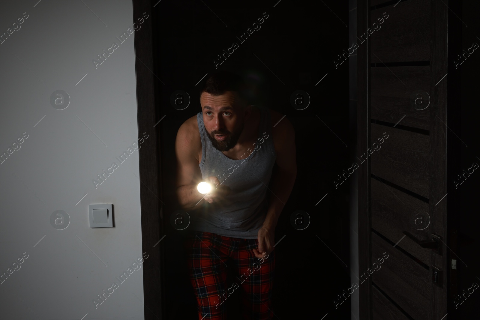 Photo of Fear of darkness. Scared man with flashlight in room at night