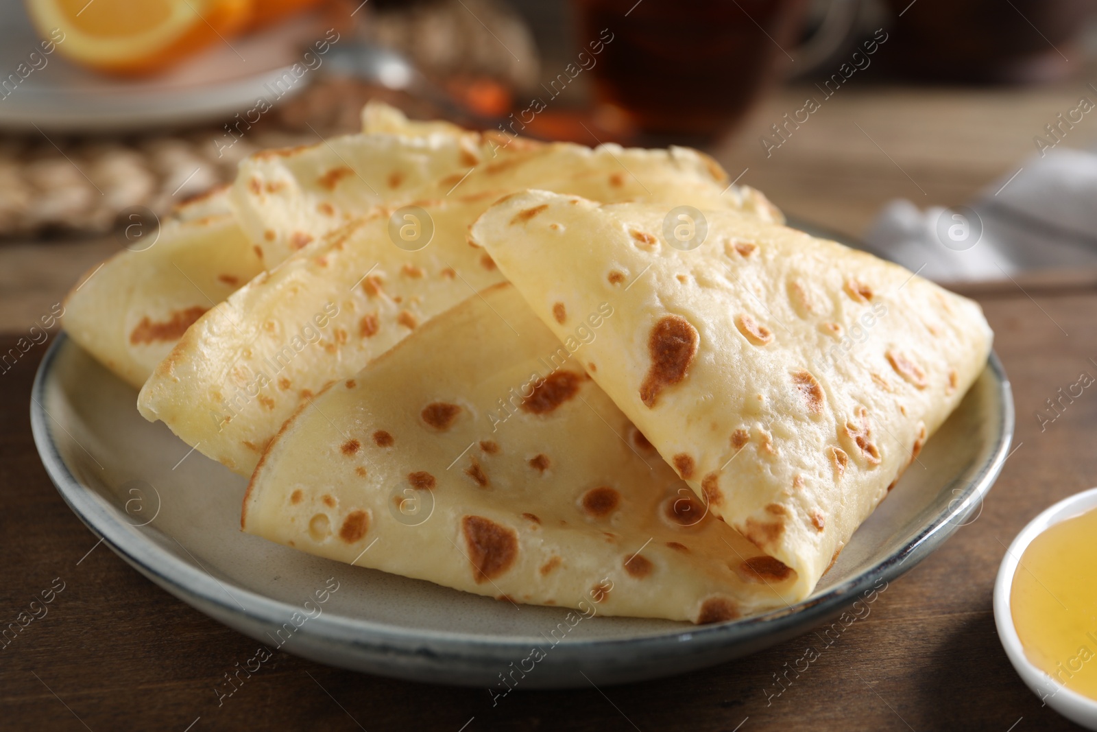 Photo of Plate with delicious folded crepes on wooden table, closeup