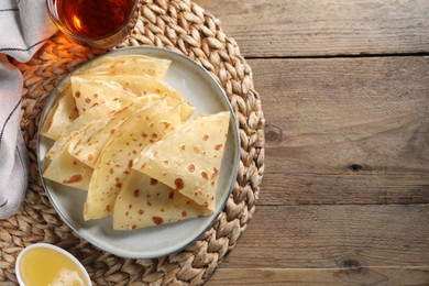 Delicious crepes, honey and tea on wooden table, flat lay. Space for text