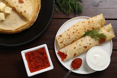 Photo of Delicious crepes with red caviar served on wooden table, flat lay