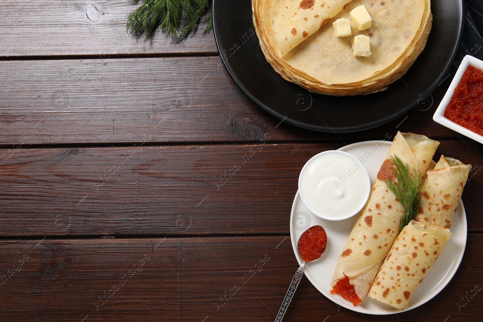 Photo of Delicious crepes with red caviar served on wooden table, flat lay. Space for text