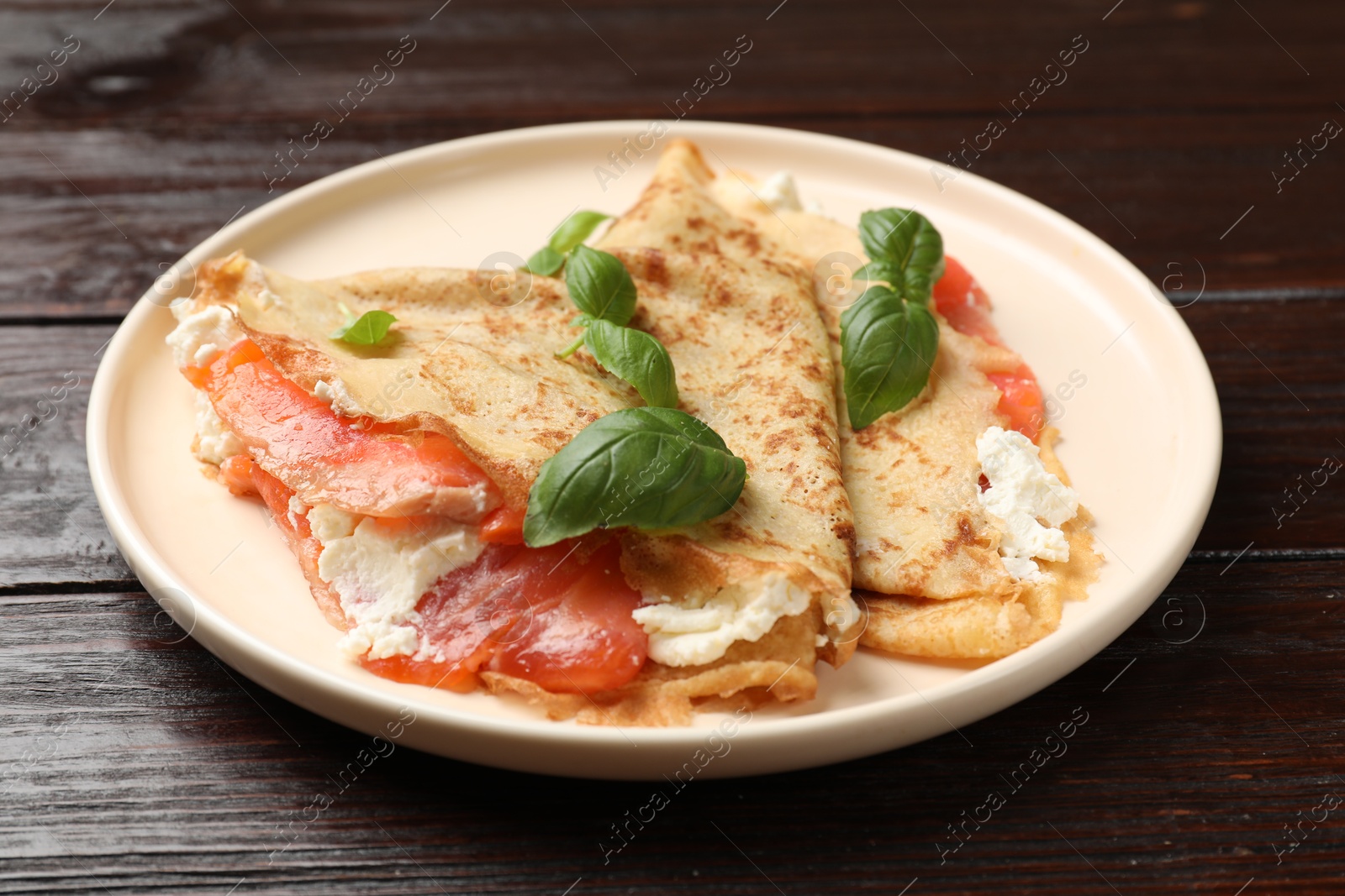 Photo of Delicious crepes with salmon, cream cheese and basil on wooden table, closeup