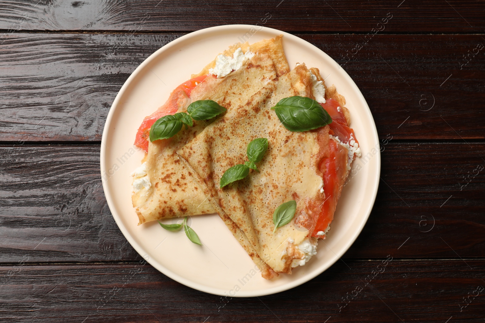 Photo of Delicious crepes with salmon, cream cheese and basil on wooden table, top view