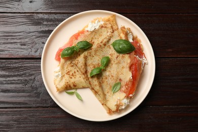 Photo of Delicious crepes with salmon, cream cheese and basil on wooden table, top view