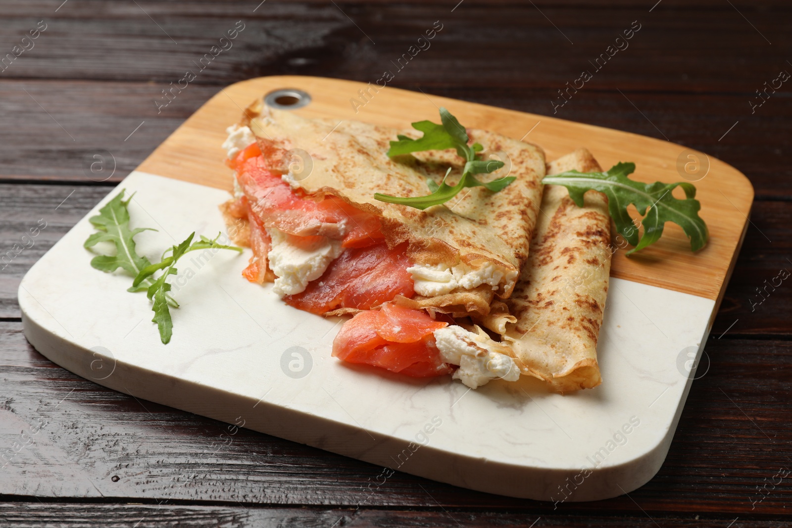 Photo of Delicious crepes with salmon, cream cheese and arugula on wooden table, closeup