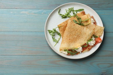 Photo of Delicious crepes with salmon, cream cheese and arugula on blue wooden table, top view. Space for text