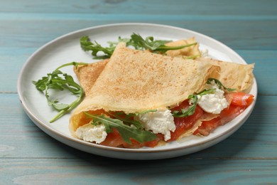 Photo of Delicious crepes with salmon, cream cheese and arugula on blue wooden table, closeup