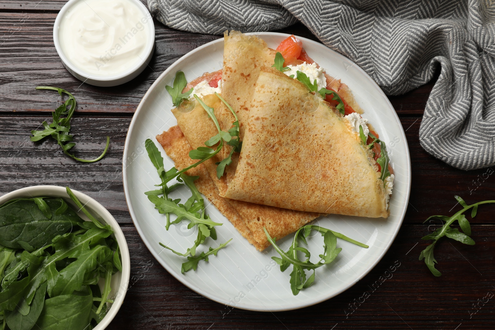 Photo of Delicious crepes with salmon, cream cheese and arugula on wooden table, flat lay