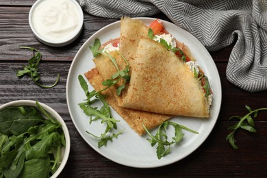 Photo of Delicious crepes with salmon, cream cheese and arugula on wooden table, flat lay