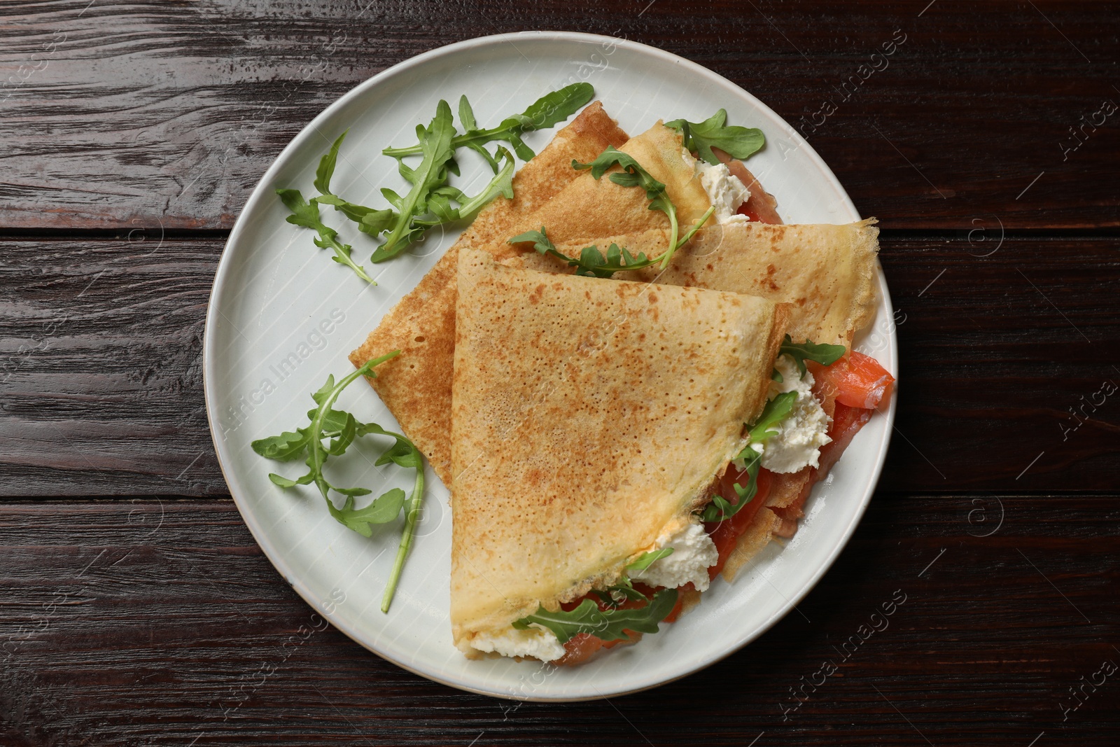 Photo of Delicious crepes with salmon, cream cheese and arugula on wooden table, top view