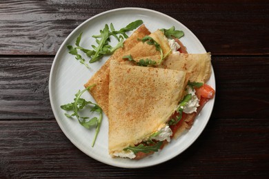 Photo of Delicious crepes with salmon, cream cheese and arugula on wooden table, top view