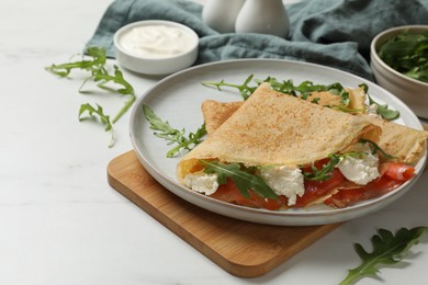 Photo of Delicious crepes with salmon, cream cheese and arugula on white table