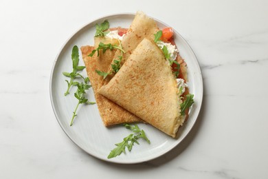 Photo of Delicious crepes with salmon, cream cheese and arugula on white marble table, top view