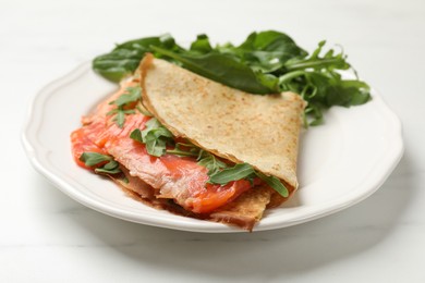 Photo of Delicious crepes with salmon and arugula on white table, closeup