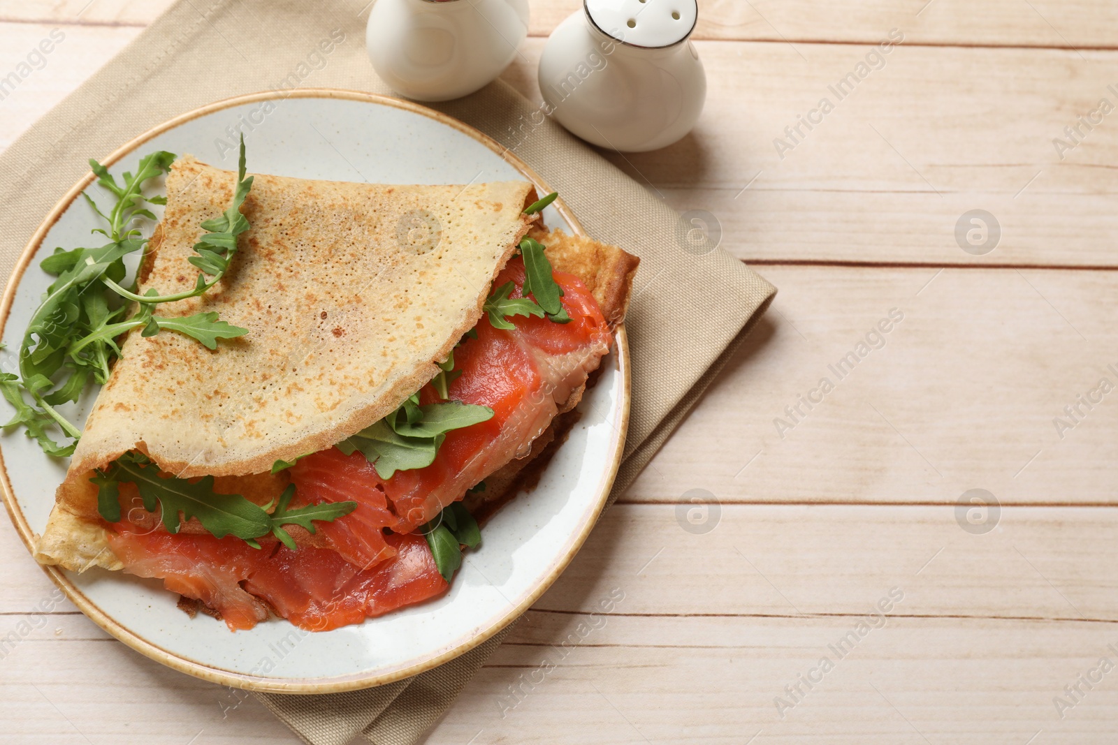 Photo of Delicious crepes with salmon and arugula on white wooden table, top view. Space for text