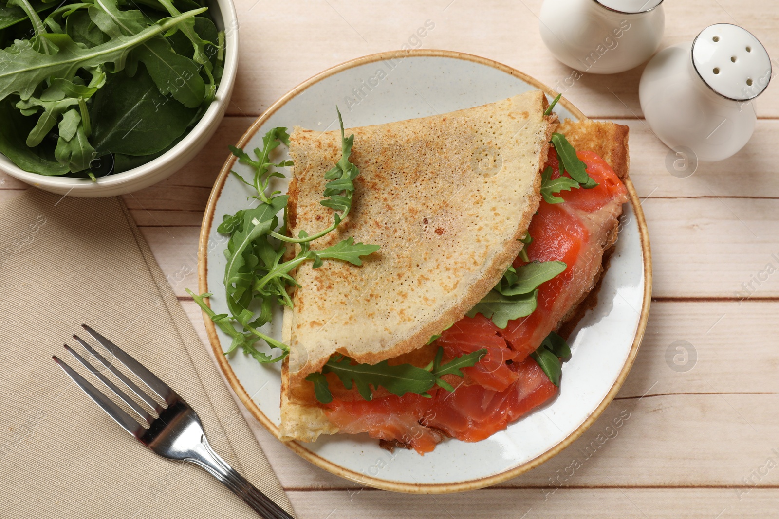 Photo of Delicious crepes with salmon and arugula on white wooden table, flat lay