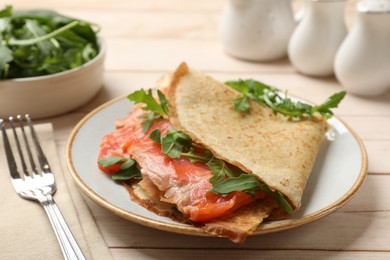 Photo of Delicious crepes with salmon and arugula on white wooden table, closeup