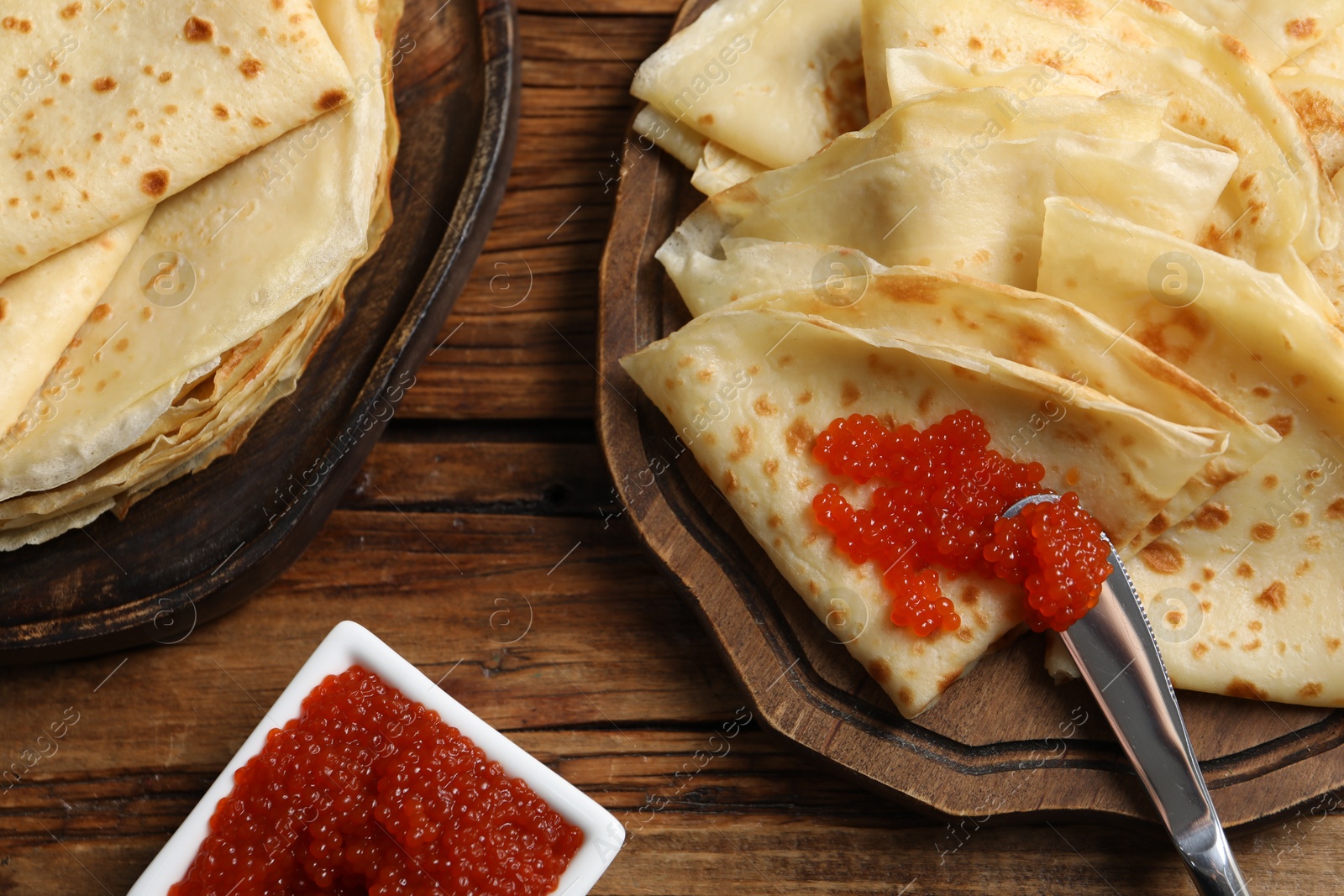 Photo of Tasty crepes and red caviar served on wooden table, flat lay