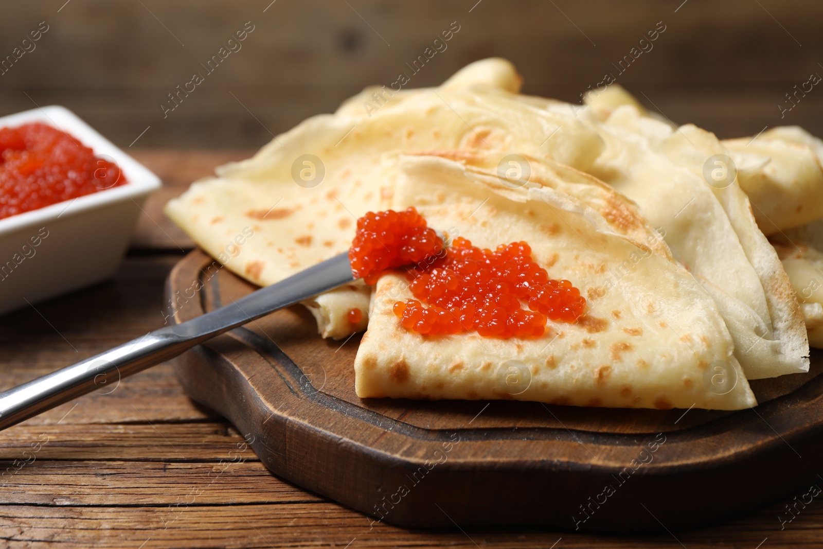 Photo of Tasty crepes and red caviar on wooden table, closeup