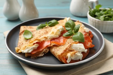 Photo of Delicious crepes with salmon, cream cheese and basil on light blue wooden table, closeup