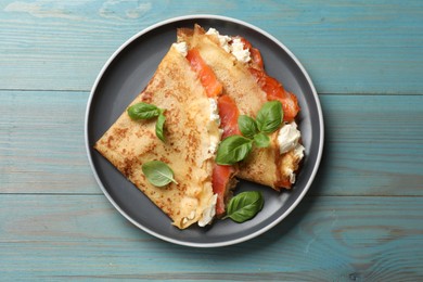 Photo of Delicious crepes with salmon, cream cheese and basil on light blue wooden table, top view