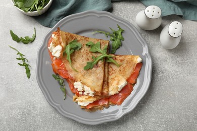 Photo of Delicious crepes with salmon, cream cheese and arugula on grey table, flat lay