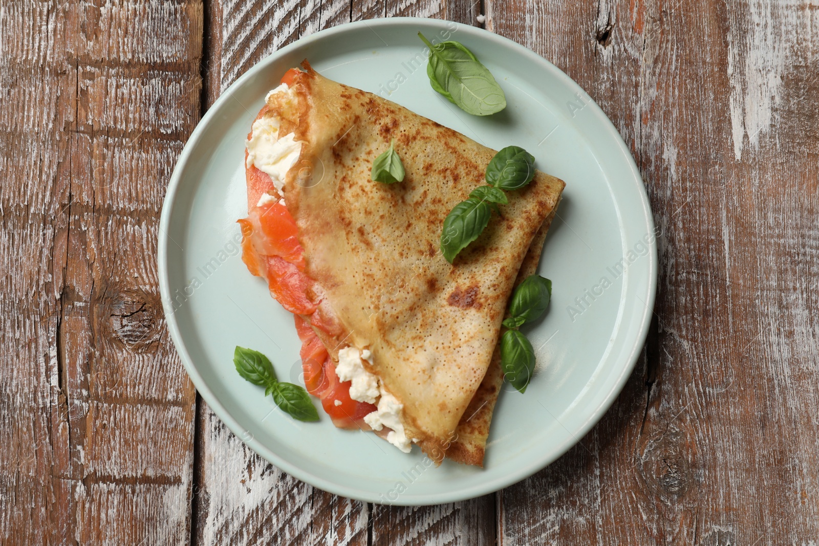 Photo of Delicious crepe with salmon, cream cheese and basil on wooden table, top view