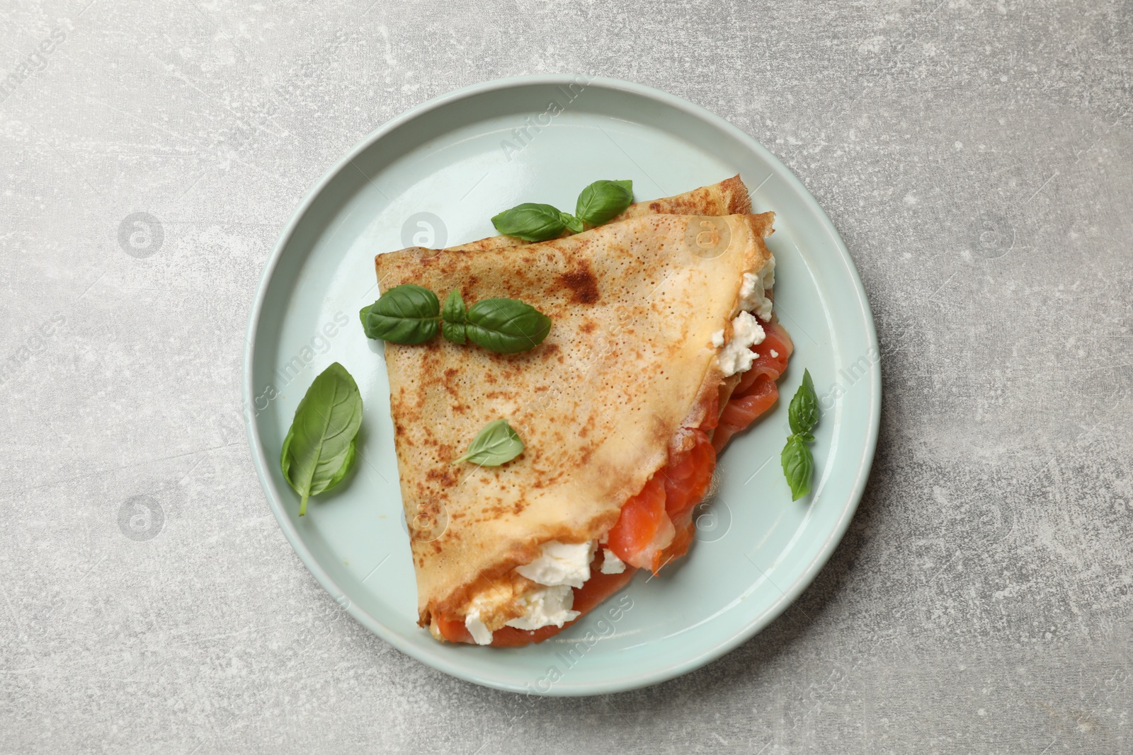 Photo of Delicious crepe with salmon, cream cheese and basil on grey table, top view